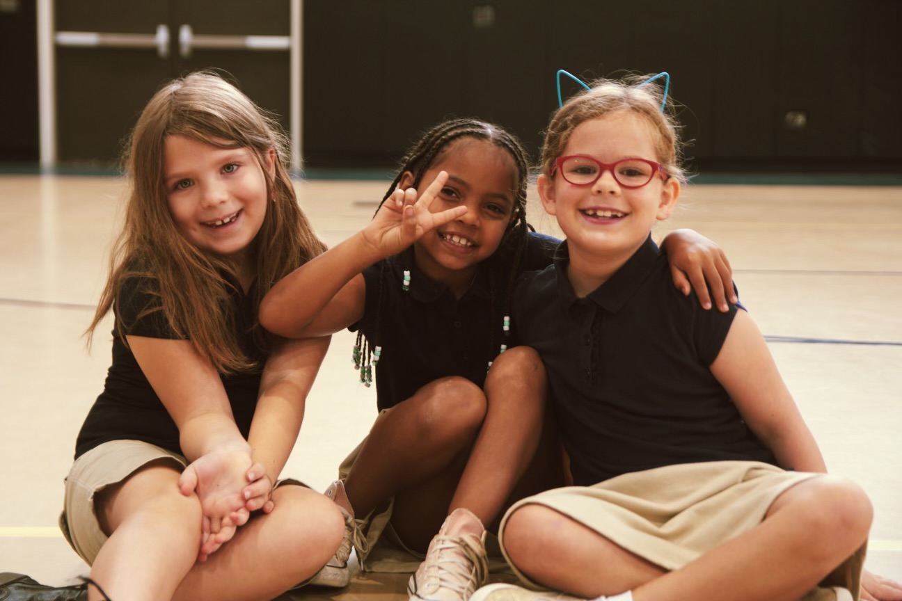 Three smiling students sitting together in the gym during the Encore after school program