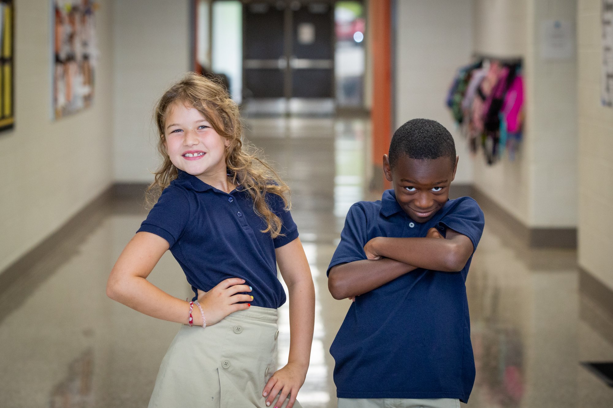 Two Westside students in navy uniform polos posing playfully in a school hallway